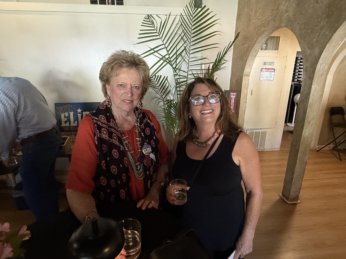 Two supporters at the launch party, one wearing a Vote Elise button, a campaign sign behind them