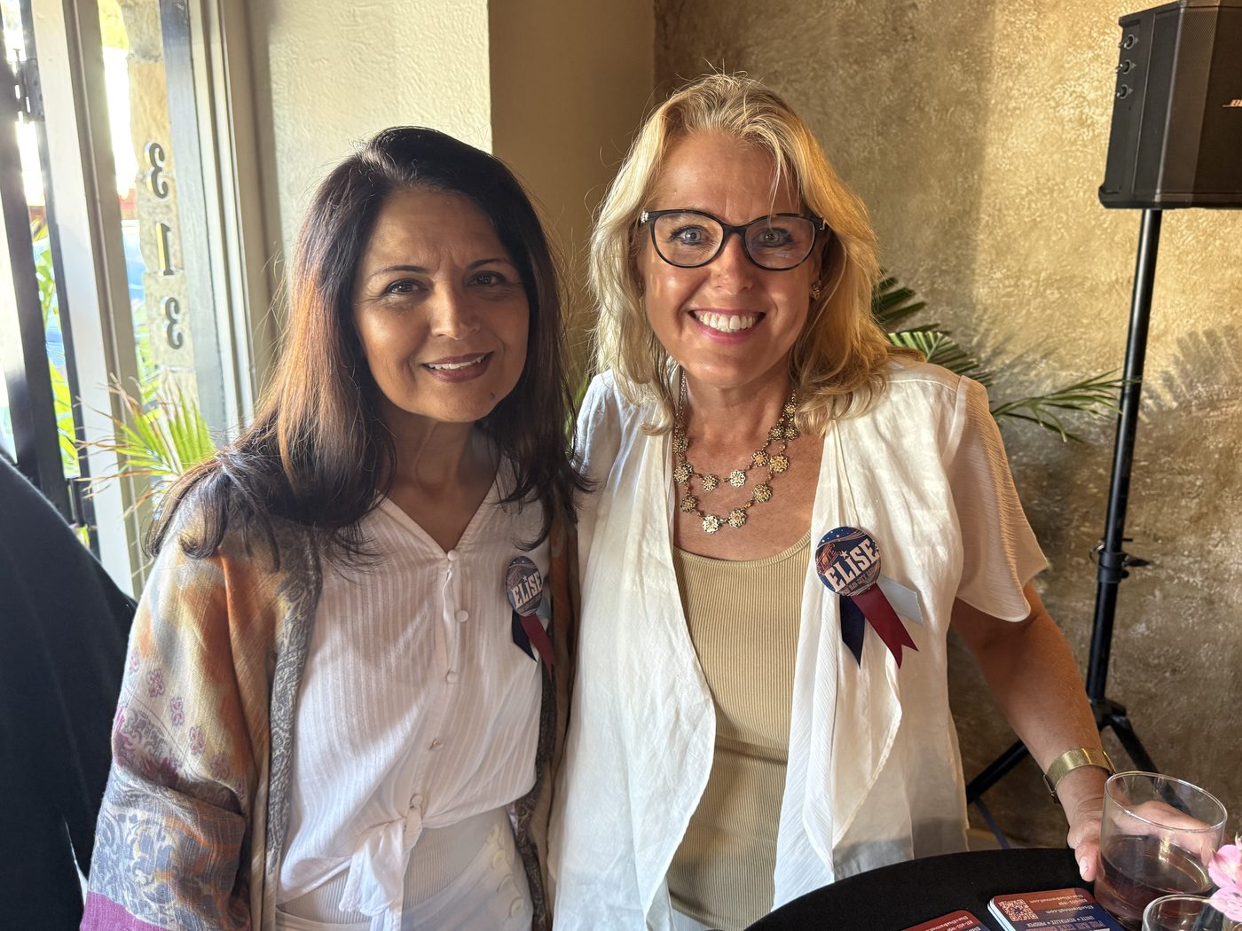 Two supporters wearing Vote Elise buttons beside a window