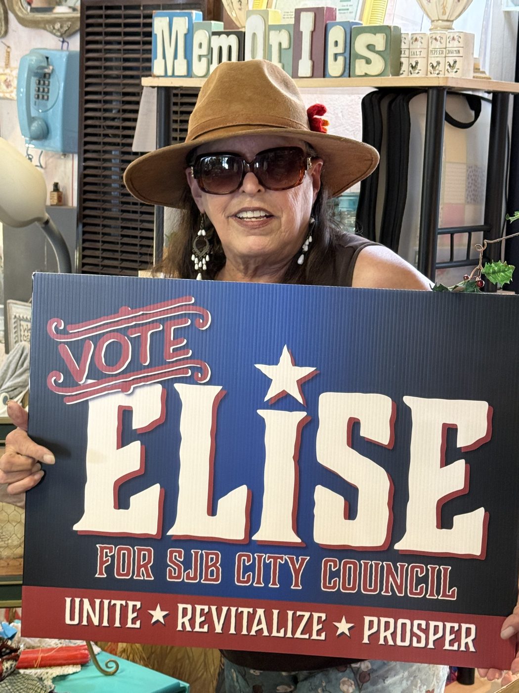 A supporter in a hat holding a Vote Elise sign inside a shop